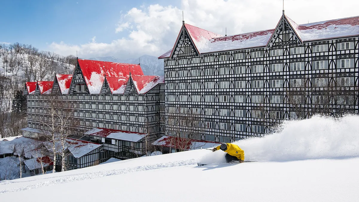赤屋根のホテルを背景に雪煙を上げて滑るスキーヤー