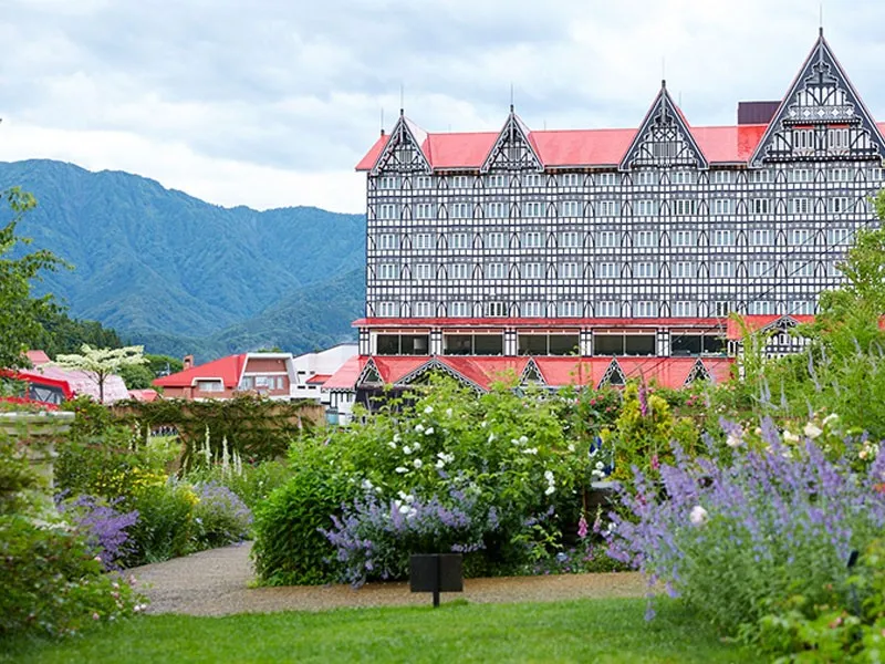 花壇と小道の先に立つ赤屋根のホテルグリーンプラザ白馬外観