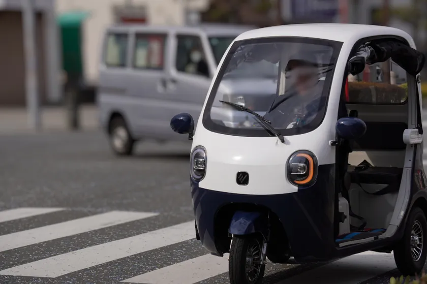 街中で走行する白とグレーの屋根付き電動トライク