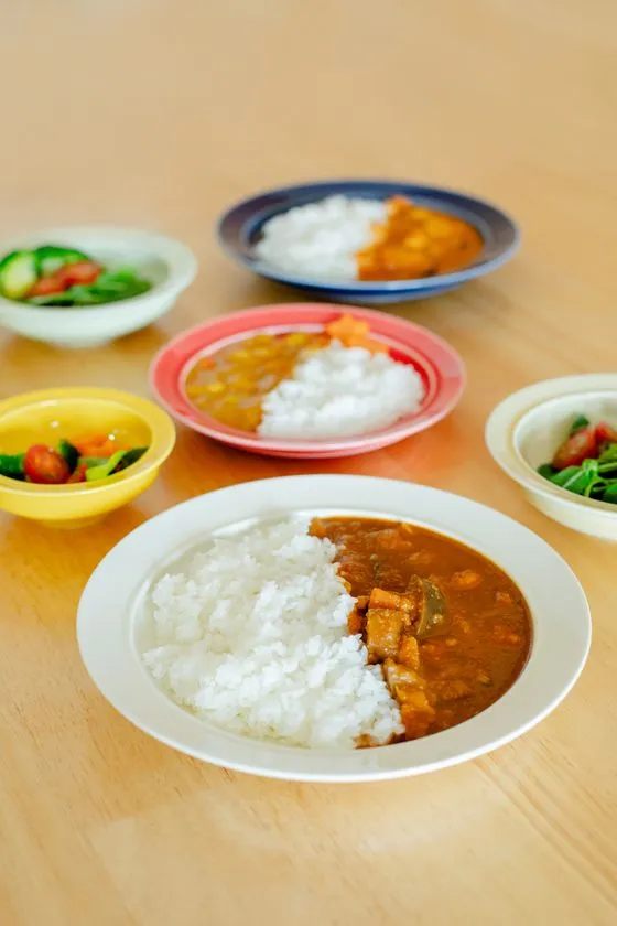 SUKUSUKU+の食器でカレーとサラダを盛り付けた食卓シーン