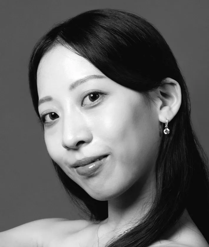 モノクロのスタジオポートレートで、黒髪をタイトにまとめた女性がやや顎を上げて凛とした視線を向けている。強調したアイメイクとパールのドロップイヤリングが気品を添え、静けさの中に芯の強さを感じさせる。舞台作品の世界観を支えるアーティストの存在感を端的に伝える一枚である。