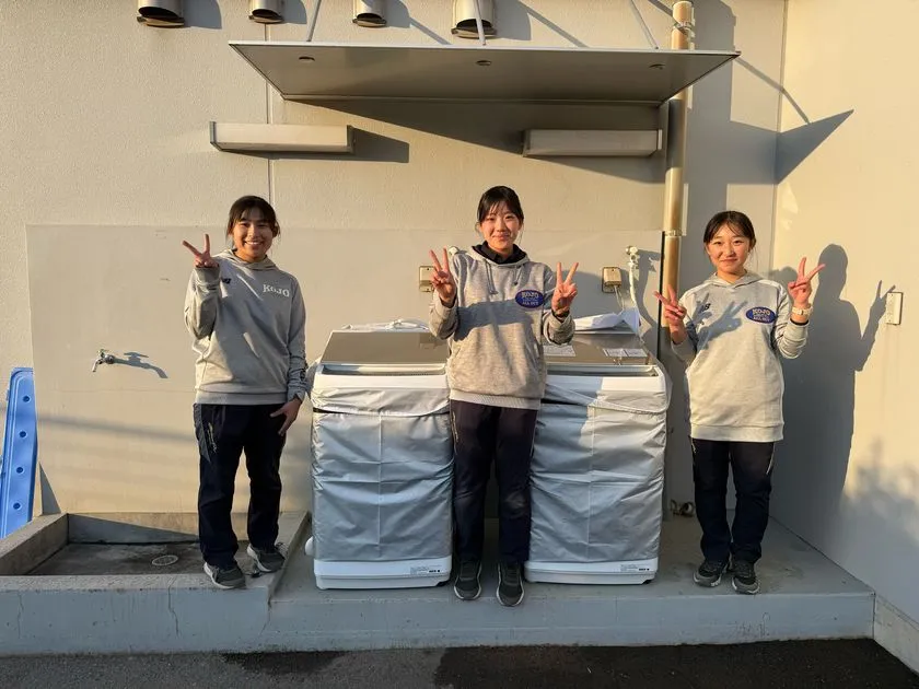 寄贈洗濯機の前でピースサインをする向上高等学校の部員
