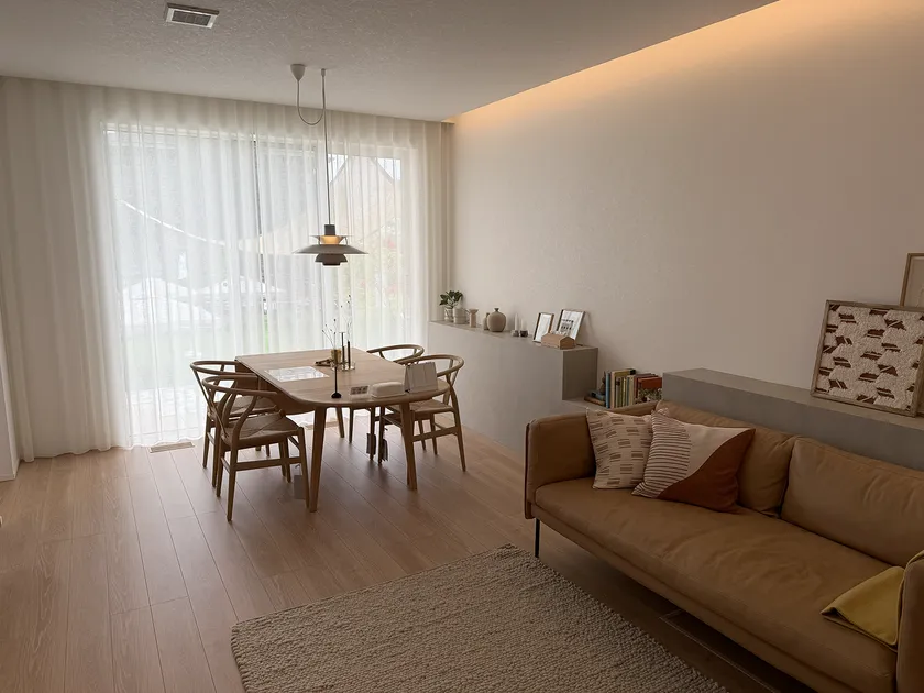 泉北ホームみのお第2展示場のリビングダイニング室内。木製ダイニングテーブルとウィッシュボーンチェア、間接照明、シアーカーテン越しの採光が見える北欧風インテリア空間