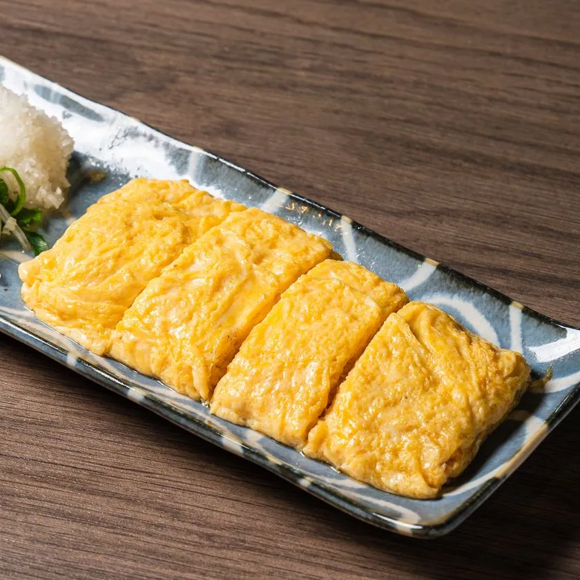 和柄の長皿に盛られた出汁巻き玉子4切れ。ふわふわの黄色い玉子焼きに大根おろしと小ねぎを添えた居酒屋定番の一品