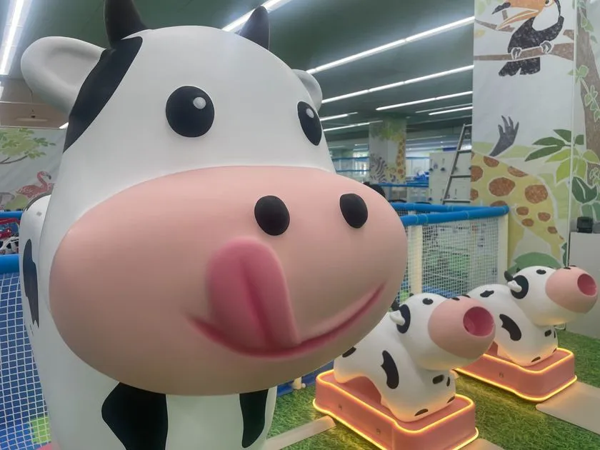 牛のキャラクター型大型オブジェとジャングル柄の壁面装飾、青いネット遊具がある牧場コーナー