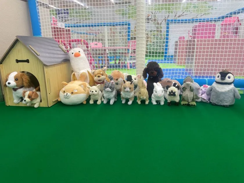 緑のカーペット上に犬、猫、うさぎ、ペンギンなど約15体の動物ぬいぐるみと木製犬小屋が並ぶ動物園コーナー