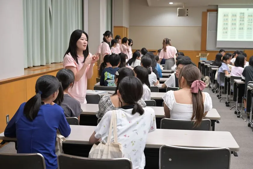 女子中高生向けセッションで登壇者がピンクTシャツ姿で参加者に語りかけ、スクリーン前の教室で交流する様子