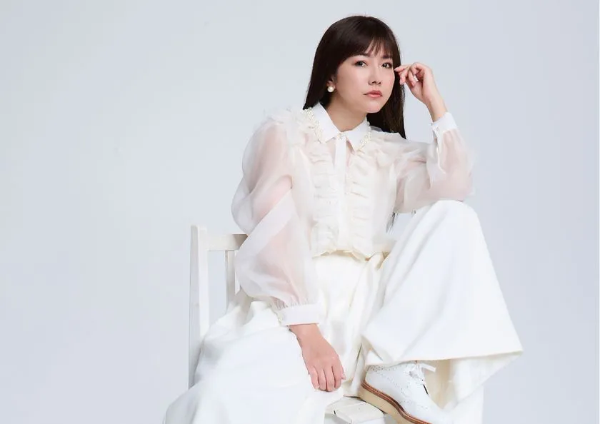 白いオーガンジーブラウスとワイドパンツ姿でフォーマルな宣材ポーズをとる島谷ひとみのスタジオポートレート
