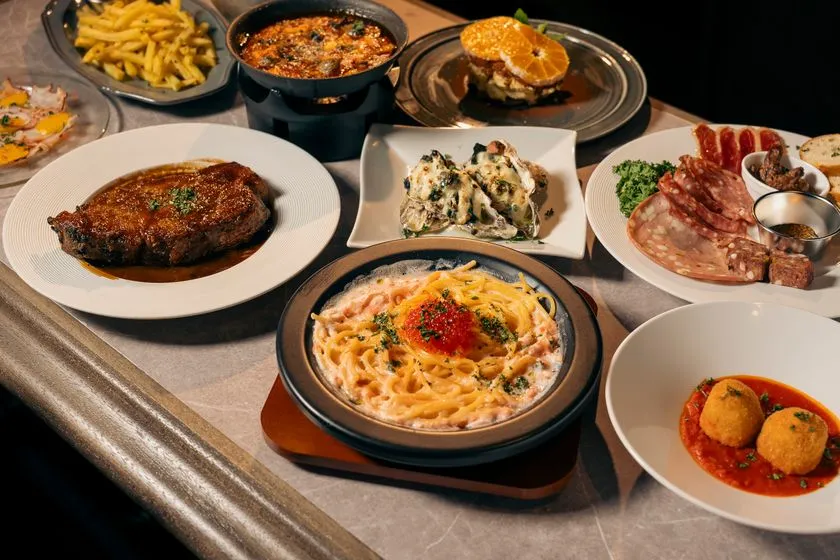 イカスミスパゲッティ・牡蠣グラタン・肉料理・生ハムサラミ盛り・アランチーニなど複数のイタリアン料理が一堂に並んだコース全体像のテーブルショット