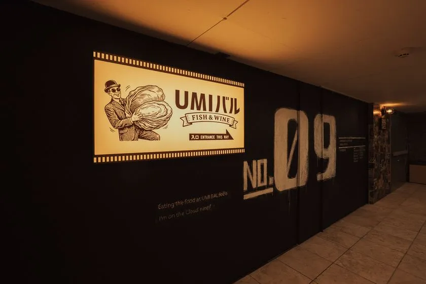 黒い壁に照らされた入口廊下に設置されたUMIバルFISH &amp; WINEのレトロ調ロゴ看板とNO.09の大型グラフィックアートの店舗エントランス写真
