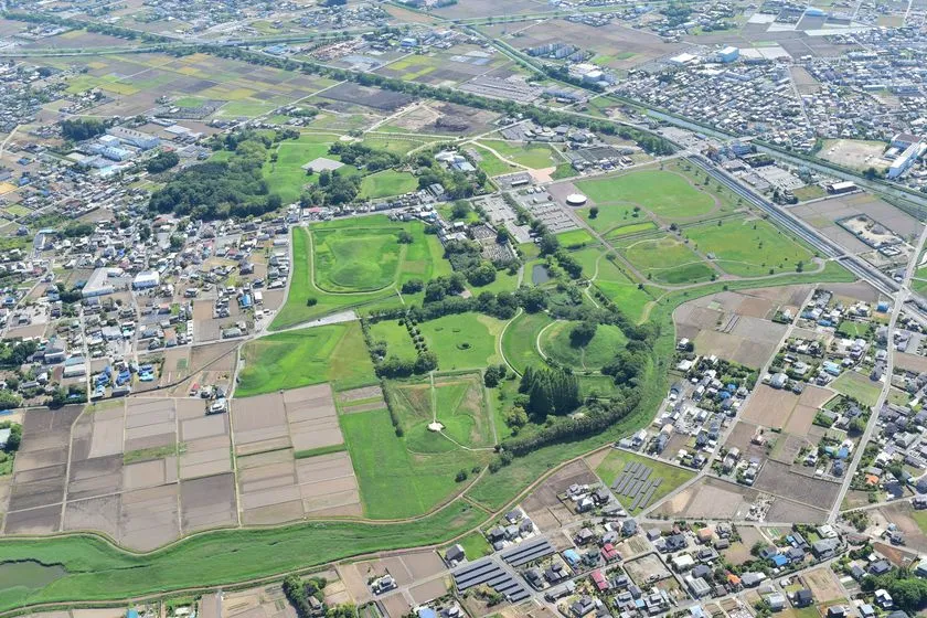 行田市の埼玉古墳群とその周辺市街地を上空から俯瞰した航空写真で、円形・前方後円形の古墳の形状と緑地規模が確認できる