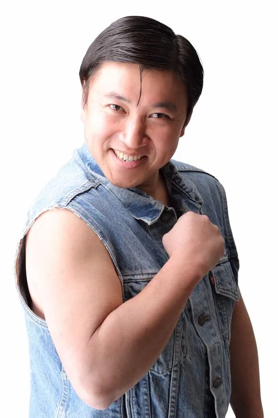袖なしデニムベストを着た男性芸人の宣材写真。白背景でガッツポーズをとっている上半身カット。