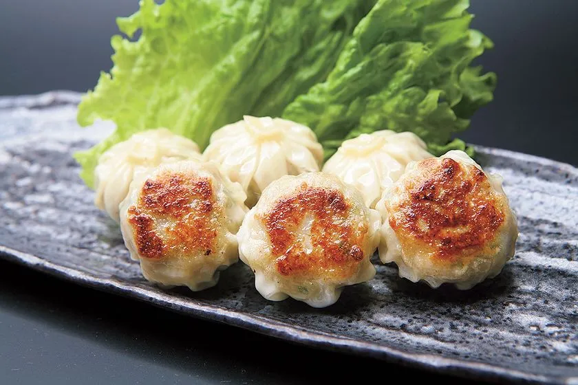 石板皿に盛られた焼きシュウマイ5個。上面がこんがりと焼き目のついた丸型シュウマイで、背後にレタスを添えた博多料理の商品写真