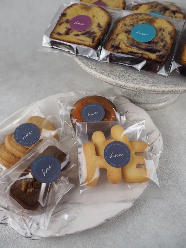 hueブランドのマーブルパウンドケーキ・クッキー・マフィン・ブラウニーなど複数種の手作り焼き菓子を個包装で並べた商品ショット。ロゴシールで統一されたパッケージ