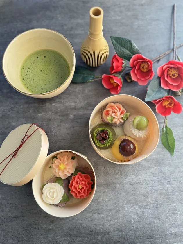 花形の和菓子を丸形木製箱2点に詰め合わせ、抹茶・茶筅・造花椿を添えた和菓子ハンドメイド作品の俯瞰ショット