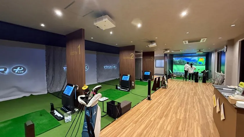 マイゴル小山店の屋内シミュレーションゴルフブース全景。BOOTH1〜3の個別打席にGOLFZON機器が設置され、利用者が実際にスイングしている様子が写る