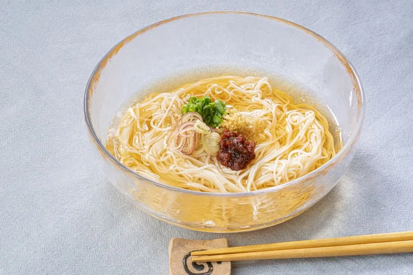 夏メシ革命をトッピングしたそうめんのガラスボウル盛り付け料理写真。薬味と辛味調味料をのせた冷たいそうめんの夏アレンジ提案カット