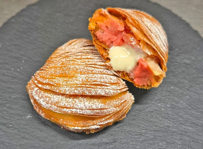 パイ生地包みの焼き菓子を半割りにした断面ショット。ピンク色のいちごクリームと白いカスタードクリームが層状に詰まった東武限定スイーツ
