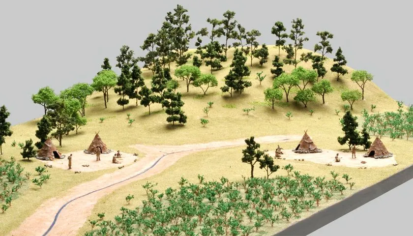旧石器時代の野営地を再現した立体模型。丘陵地に樹木が配置され、3か所の円錐形テント（ティピー状住居）と人物フィギュアが小径沿いに点在する復元ジオラマ。