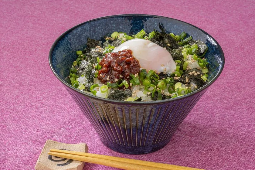 鬼うま！夏メシ革命をご飯の上にのせた丼アレンジ。温泉卵・刻み海苔・小ねぎ・ごまをトッピングした盛り付け例で青い陶器のボウルに盛られている