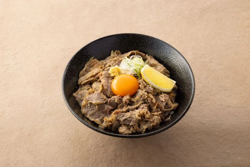 絵空事Fビレッジ店の玄米うどんを使った牛肉丼風メニュー。黒い丼鉢に薄切り牛肉・卵黄・ネギ・レモンを盛りつけた一品。