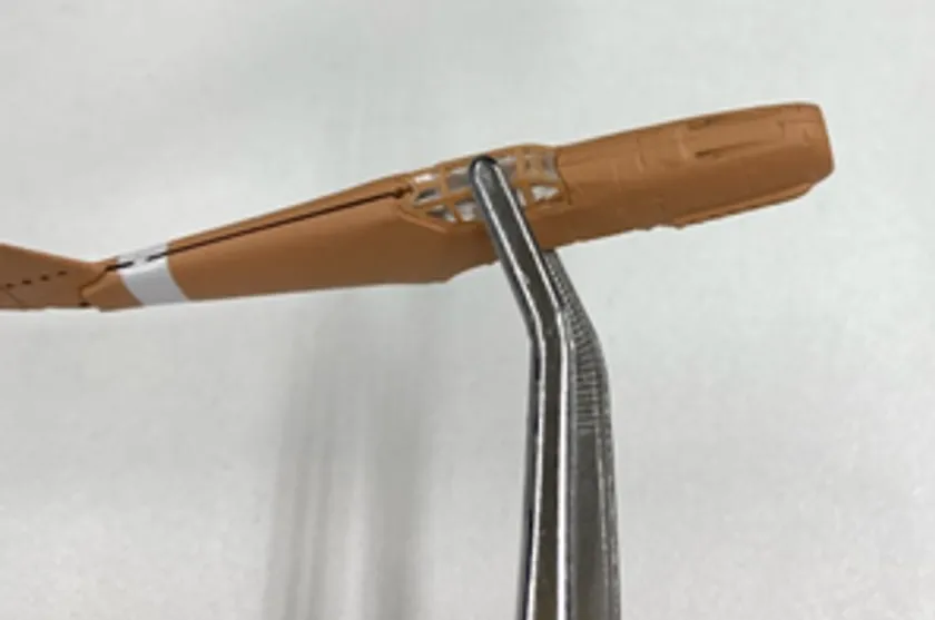 プラモデル製の飛行機部品(茶色)の接合部に金属製ピンセットを差し込んでいる組み立て工程のアップショット