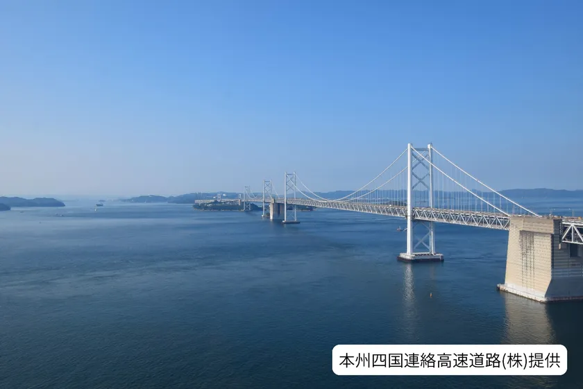 瀬戸大橋を側面から捉えた全景写真で、島々と穏やかな海面が広がる。本州四国連絡高速道路株式会社提供のクレジット入り