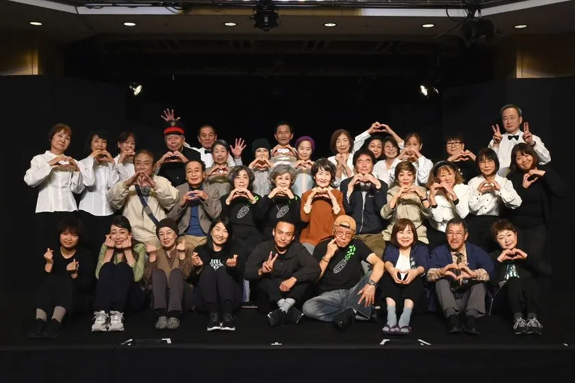 劇団すずしろの全メンバー約30名がステージ上でハートポーズをとる集合写真。シニア中心の劇団員構成がわかる黒背景のホール内での撮影。