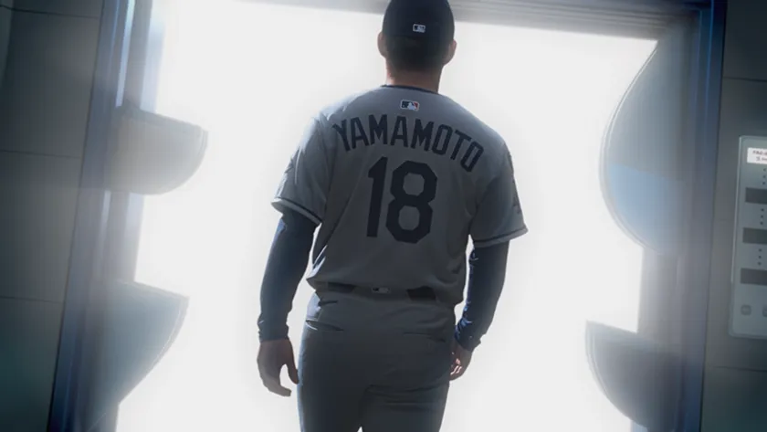 背番号18・YAMAMOTO表記のドジャースアウェーユニフォーム姿の山本由伸投手が、エレベーターのドアが開く逆光の中に立つ後ろ姿のCMカットショット