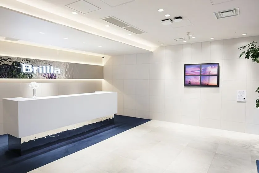 Brilliaギャラリーの白基調エントランス内観で、受付カウンター左壁面のアート作品と正面白壁に額装された写真作品の展示状態を撮影した室内写真