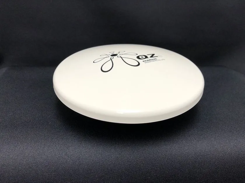 小峰無線電機のGNSSアンテナ製品「OZ」シリーズと思われる円盤型白色筐体の単体商品ショット。KOMINEブランドロゴと型番表記が天面に入り、黒背景で撮影された正面斜め上からのカット