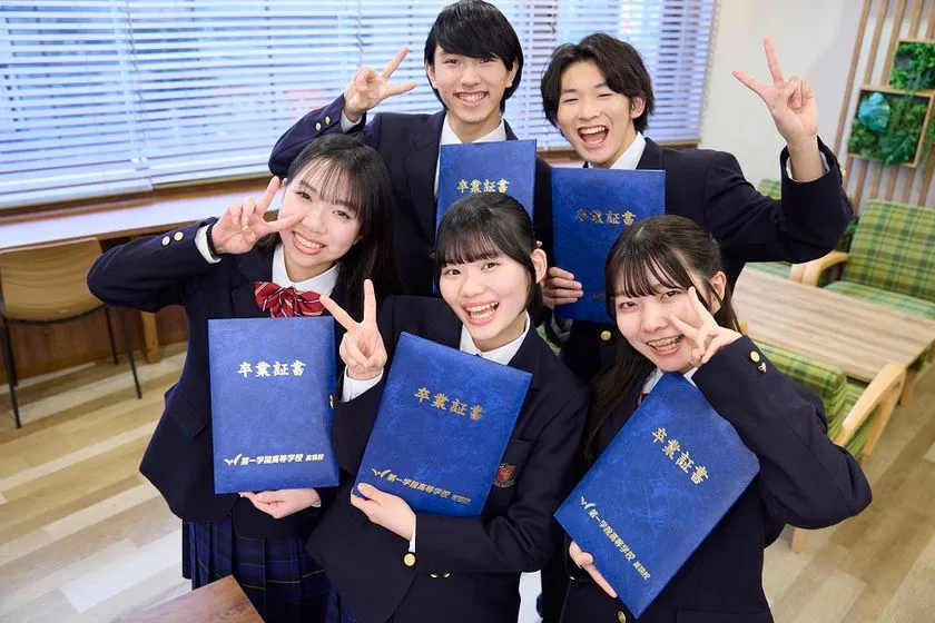 第一学院高等学校の制服を着た男女5名の生徒が「第一学院高等学校」のロゴ入り青い卒業証書フォルダーを手に持ちピースサインで笑顔を見せる集合写真