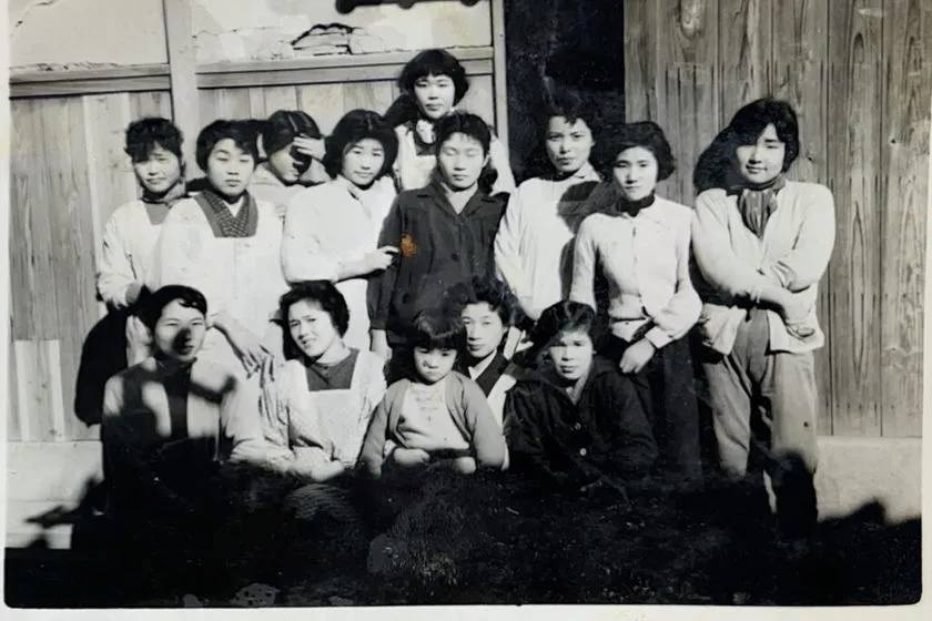 昭和期と思われるモノクロ集合写真で、木造建物前に女性従業員約12名が前後2列で並ぶ南出メリヤス創業当時の工場スタッフ写真
