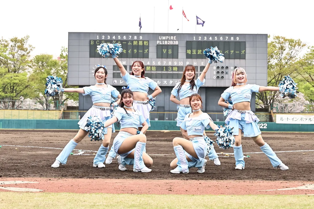 BCリーグオールスターゲーム開催予定の埼玉県営大宮公園野球場のスコアボード前で、水色ユニフォームのチアリーダー7名がポンポンを持ちポーズをとる集合写真