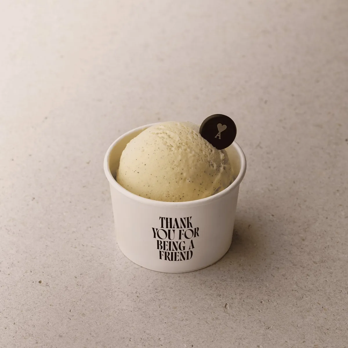 Ami Parisロゴ入りチョコレートプレートを添えたバニラアイスクリーム1スクープ、白カップに「THANK YOU FOR BEING A FRIEND」印字