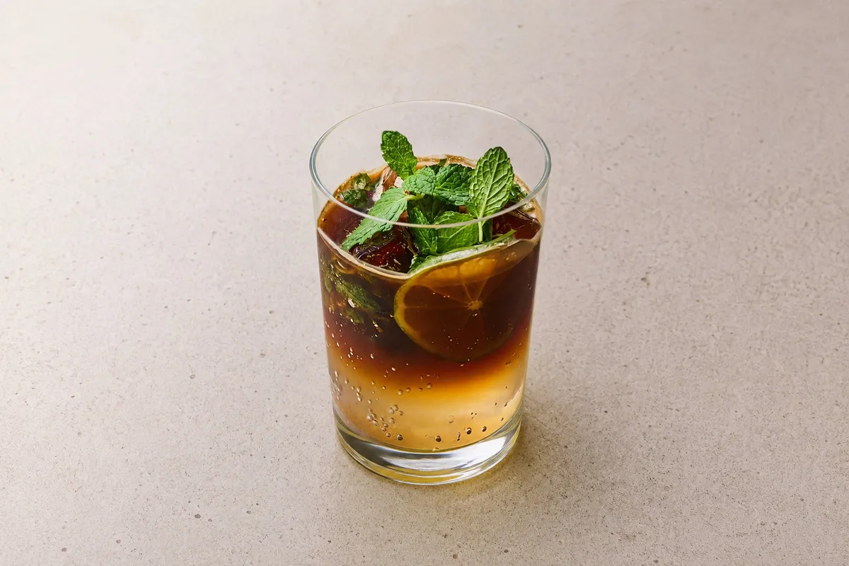 グラスに注がれたアイスコーヒーカクテル。ライムスライスとフレッシュミントをトッピングし、上層が濃い茶色・下層がオレンジ色に分かれた2層グラデーションのコールドドリンク
