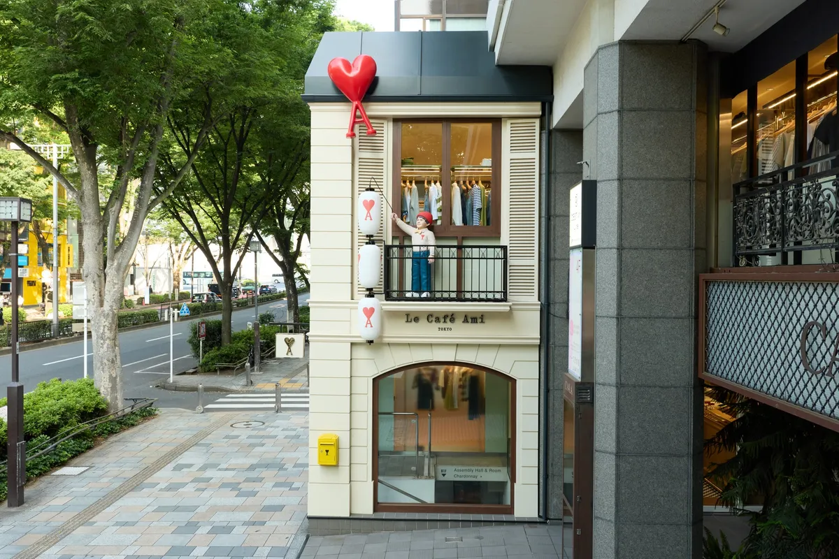 Ami Paris表参道ポップアップ「Le Café Ami TOKYO」の外観全体。屋上に赤いハートのAロゴ風船、バルコニーに人形フィギュア、2階に衣類ディスプレイが見える白壁の2階建て店舗外観