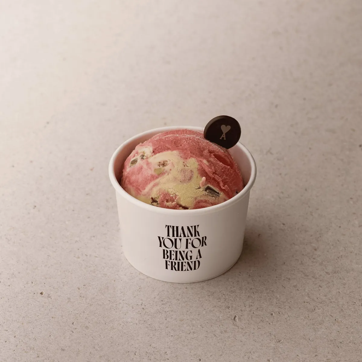 Ami Parisロゴ入りチョコレートプレートを添えたストロベリーマーブルアイスクリーム1スクープ、白カップに「THANK YOU FOR BEING A FRIEND」印字
