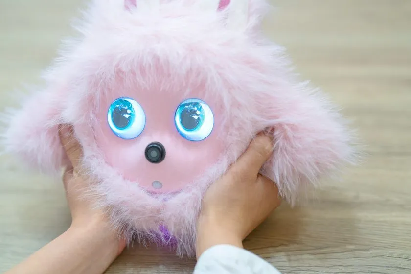 KOTTIピンクモデルを子どもの両手で持つクローズアップショット。青く光るLEDアイとカメラ内蔵ノーズの構造が正面から確認できる