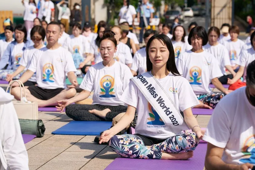 Japan Miss World 2021のたすきを付けた女性が屋外でヨガのポーズをとる参加者クローズアップショット、国際ヨガの日ロゴ入りTシャツ着用