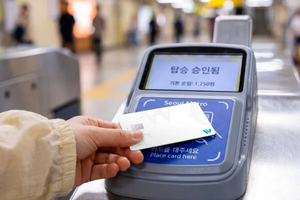 ソウル地下鉄の改札機にTravel Walletカードをタッチしている場面。画面に「탑승 승인됨（乗車承認）基本運賃1,250ウォン」と表示され、実際の交通決済シーンを示す。