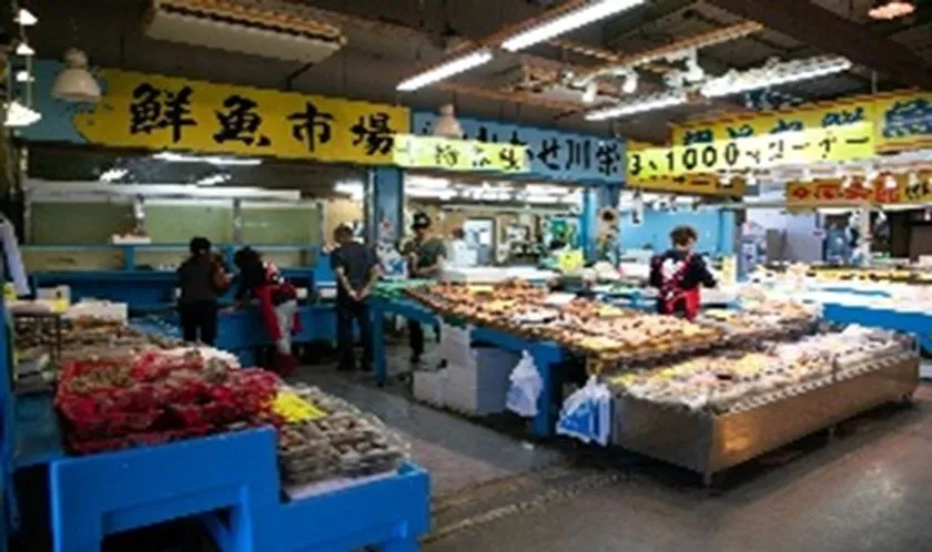 鮮魚市場の店内全景。「鮮魚市場」の黄色い看板が掲げられ、貝類や干物が陳列された販売台に複数の客とスタッフが立っている