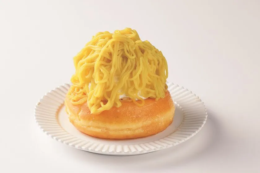 白い丸皿に載ったドーナツ型パンの上に、細麺状モンブランクリームを山盛りに絞ったスイーツの商品写真。黄色みのある栗クリームが麺状に盛られビジュアルインパクトが強い