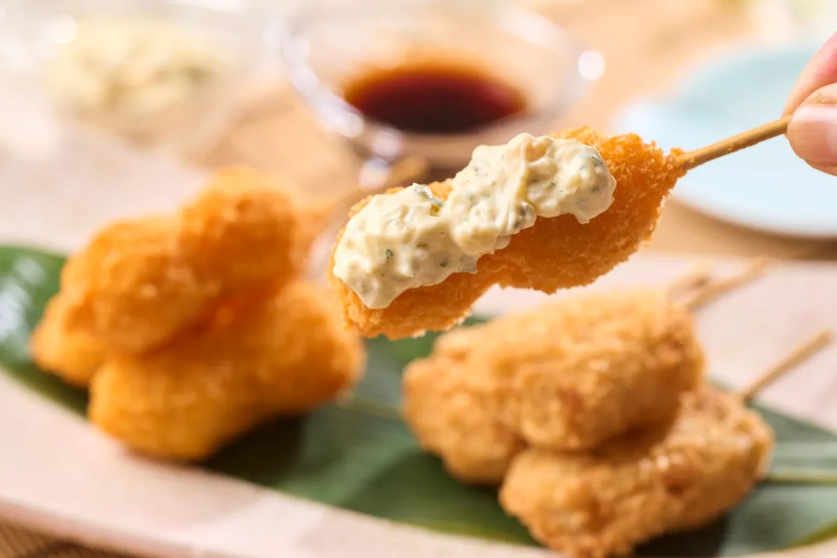 串揚げとエビフライにタルタルソースをたっぷりかけた揚げたて天ぷら串の料理写真。醤油ダレの小皿と複数の揚げ物が盛り合わせで登場