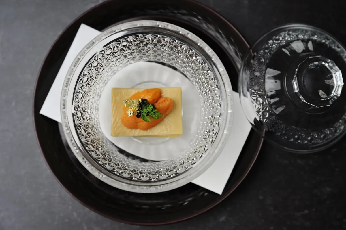 クリスタル皿に盛られたウニとキャビアの前菜料理。薄いクレープ状の台座に橙色のウニを乗せ、金箔とキャビアをあしらい、パセリを添えた一品
