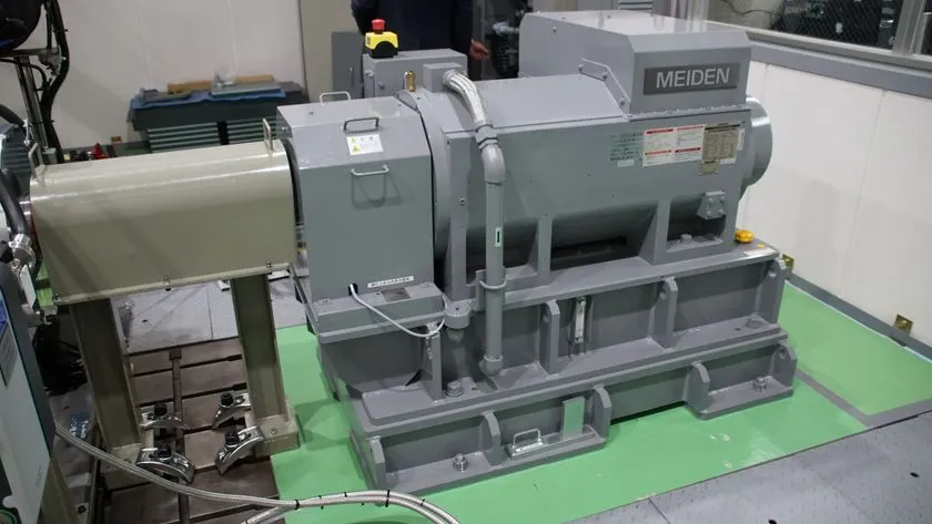 愛知碧南R&DセンターのMEIDEN製大型発電機・試験装置を室内で撮影した写真。グレー色の本体とマウント台座、配線類が確認でき、水素燃焼エンジン研究用の動力計測設備とみられる