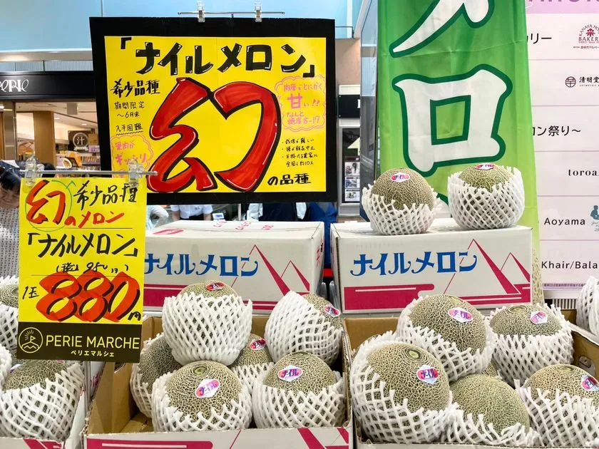 希少品種ナイルメロン1玉880円の値段POP拡大ショット。幻の品種と赤字で強調した黄色手書きPOP・ペリエマルシェロゴ入り価格札・ネット包装のメロン山積みが写っている