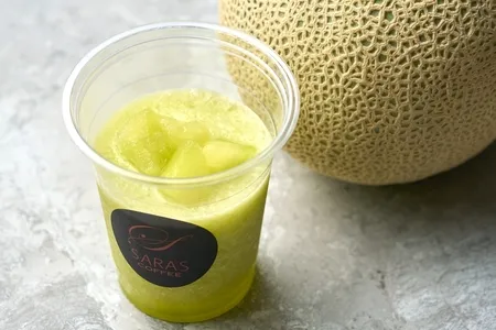SARA'S COFFEEブランドのプラスチックカップに入ったメロンスムージーと、隣に置いた丸ごとメロン1個。田原産メロンを使用したドリンク商品の単品ショット