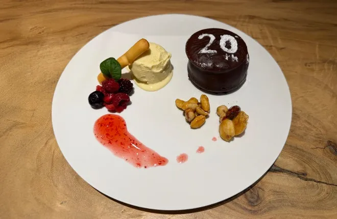 白皿に盛られた20周年記念デザートプレート。チョコレートケーキに「20th」と記され、バニラアイス・ベリー・ナッツ・ラズベリーソースを添えた構成