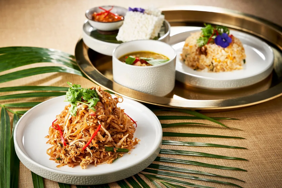パッタイ(炒め米麺)、グリーンカレー、炒飯、ライスなど複数のタイ料理がシルバートレーと白皿に盛り付けられた料理集合ショット